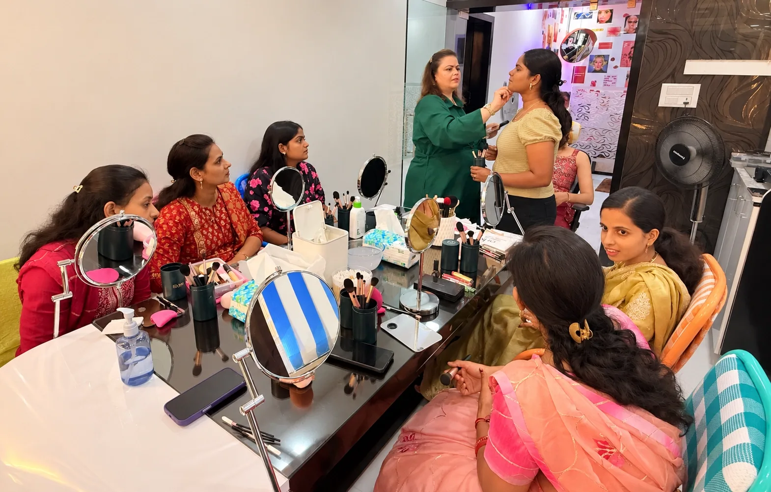 Students practising at mirrored vanity tables while Rekha guides a student at the back of the studio